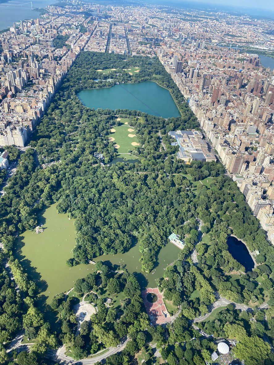 Central Park unfolds below, a lush oasis amidst the city's skyline, viewed from a helicopter, offering a breathtaking perspective of nature's sanctuary in the heart of New York City.