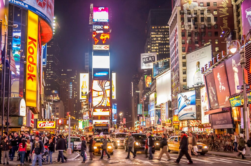Times Square: Iconic New York Cityscape, adorned with vibrant stores, dazzling neon lights, and a bustling crowd of locals and tourists, epitomizing the electric energy of the Big Apple.