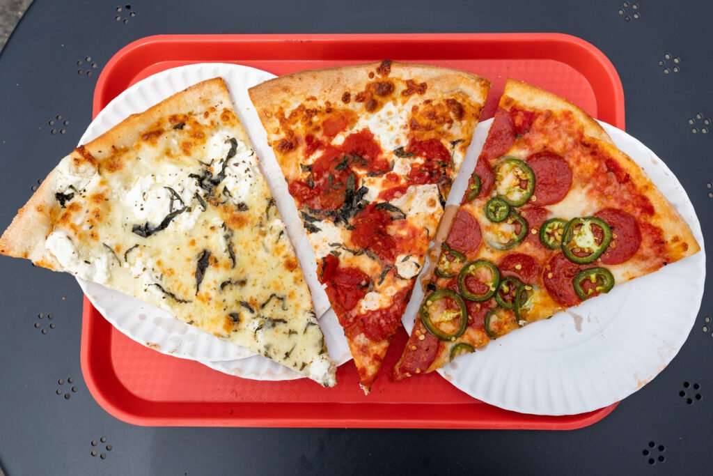 Three slices of authentic New York City style pizza rest on a vibrant red tray, tempting with their cheesy goodness and iconic thin crust, a savory snapshot of the city's culinary culture.