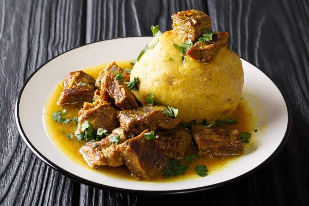 A close-up shot captures the tantalizing allure of spicy mofongo, adorned with plantains, garlic, and chicharron, accompanied by succulent meat and savory broth, presented elegantly on a table, horizontal and inviting.